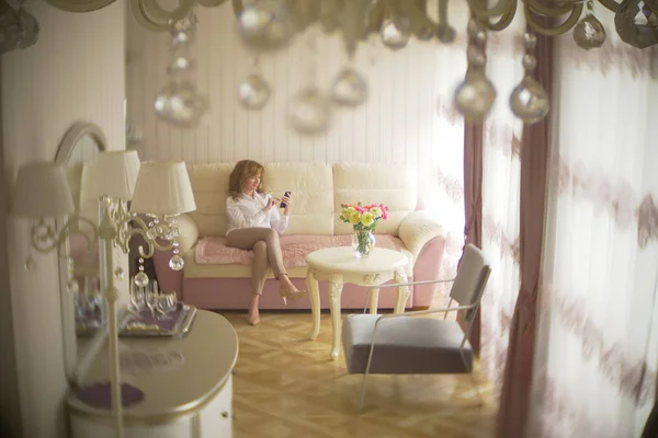 Een trendy dame gekleed in een witte blouse en een beige broek. Een jonge vrouw maakt gebruik van een mobiele telefoon binnenshuis met een prachtige interieur. — Stockfoto