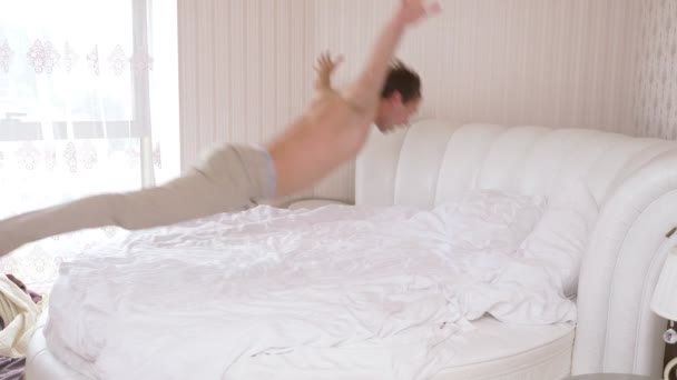 Handsome young caucasian man jumping on the bed in the bedroom. 4k, slow motion. — Stock Video