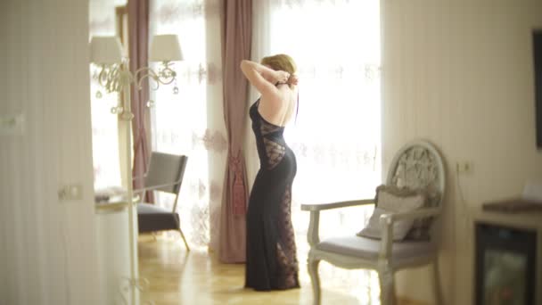 Модна леді одягнена в вечірню чорну мереживну сукню. Молода жінка позує в чуттєвій позі, тримаючи рожеві пухнасті наручники в кімнаті з вишуканим інтер'єром. 4k — стокове відео