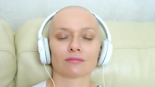 Primer plano. una mujer calva con auriculares escucha música y mueve la cabeza al ritmo de la música . — Vídeos de Stock