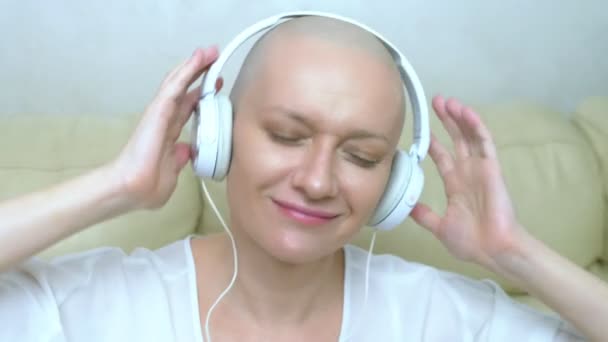 Gros plan. une femme chauve dans un casque écoute de la musique et bouge la tête au rythme de la musique . — Video