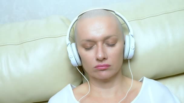 Detailní záběr. plešatá žena ve sluchátkách poslouchá hudbu a pohybuje hlavou do rytmu hudby. — Stock video