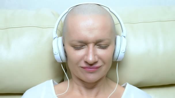 Närbild. en skallig kvinna i hörlurar lyssnar på musik och flyttar huvudet till rytmen av musiken. — Stockvideo