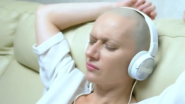 Detailní záběr. plešatá žena ve sluchátkách poslouchá hudbu a pohybuje hlavou do rytmu hudby. — Stock video