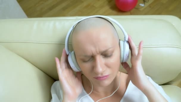 Κοντινό πλάνο. Μια φαλακρή γυναίκα με ακουστικά ακούει μουσική και κουνάει το κεφάλι της στο ρυθμό της μουσικής. — Αρχείο Βίντεο