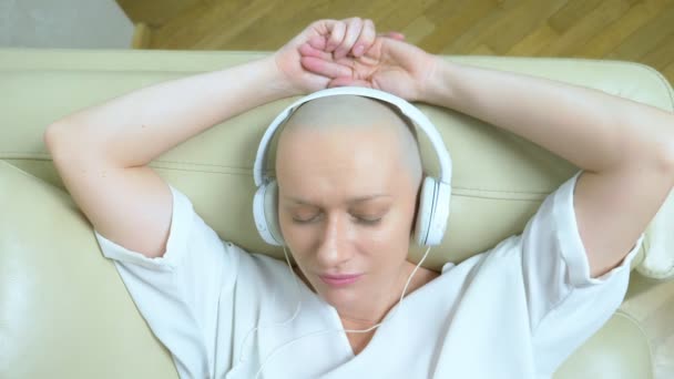 Close-up. een kale vrouw in een koptelefoon luistert naar muziek en beweegt haar hoofd op de beat van de muziek. — Stockvideo
