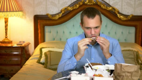 Hombre de negocios guapo está comiendo comida rápida sentado en la cama en un interior de lujo . — Vídeo de stock