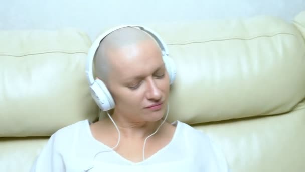 Närbild. en skallig kvinna i hörlurar lyssnar på musik och flyttar huvudet till rytmen av musiken. — Stockvideo