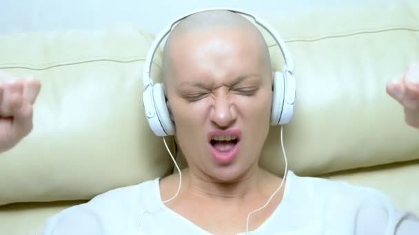 Yakın plan. Kulaklıklı kel bir kadın müzik dinler ve kafasını müziğe göre hareket ettirir.. — Stok video
