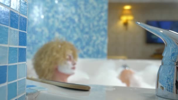 Jeune femme en masque cosmétique prend un bain avec de la mousse — Video