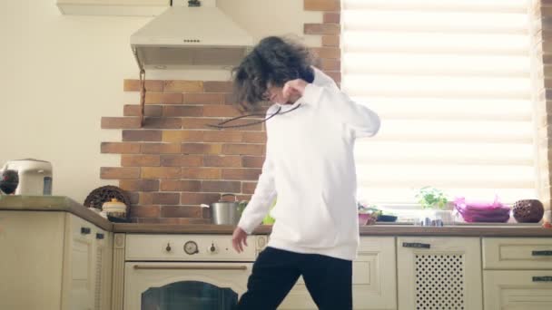 Gelukkig knap tiener jongen met lange krullend haar dansen in de keuken. — Stockvideo