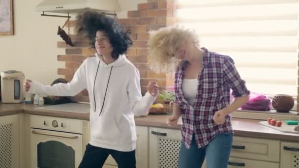 陽気ブロンドの女性は彼女の魅力的な十代の息子と時間を費やしています.彼らは台所で踊って笑っている. — ストック動画