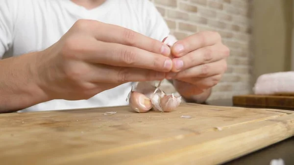 A man peels garlic sitting at a table on a background of a brick wall. — Stock Photo, Image