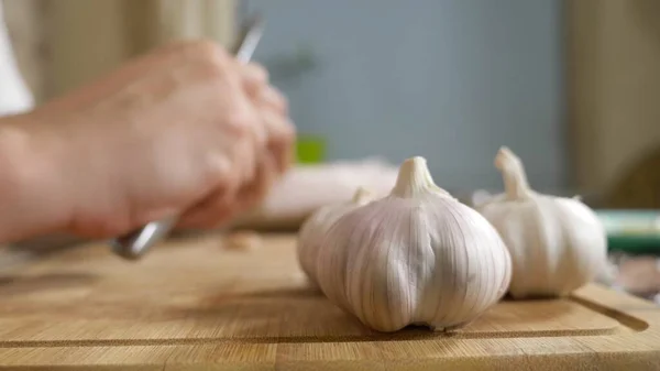 Cabeça de close-up de alho, mãos masculinas descascar o alho em uma placa de madeira — Fotografia de Stock