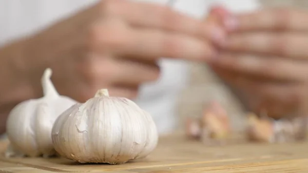Closeup κεφάλι του σκόρδου, αρσενικά χέρια ξεφλουδίσει το σκόρδο σε μια ξύλινη σανίδα — Φωτογραφία Αρχείου