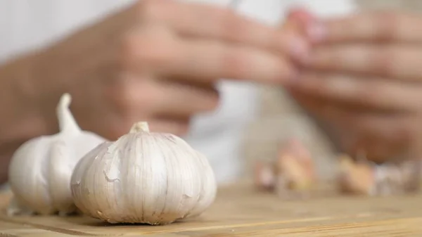 Close-up kop van knoflook, mannelijke handen schillen de knoflook op een houten plank — Stockfoto