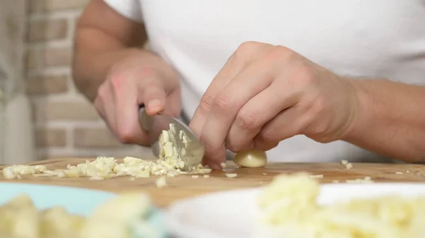 Mani maschili tagliano l'aglio su una tavola di legno. primo piano — Foto Stock