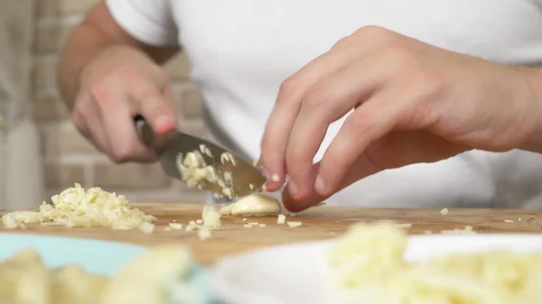 Mani maschili tagliano l'aglio su una tavola di legno. primo piano — Foto Stock