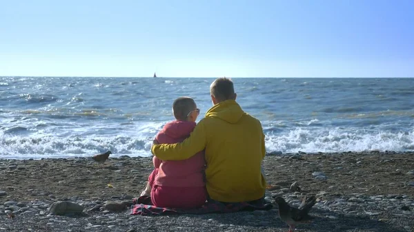 Couple en amour homme et une femme chauve sont assis sur le bord de la mer par temps frais et venteux . — Photo