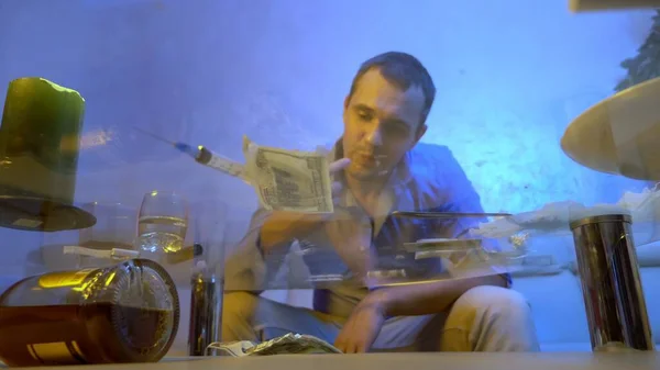 Een jongeman in een kantoorshirt wrijft wit poeder in zijn tandvlees terwijl hij op een bank in de woonkamer zit, kijkend door een glazen aanrecht — Stockfoto