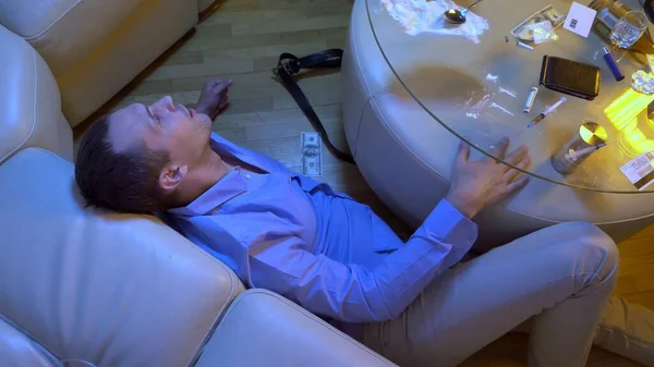 Um jovem experimenta alucinações de tomar drogas e álcool enquanto está deitado no chão ao lado de uma mesa na sala de estar . — Fotografia de Stock