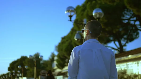 Élégante fille chauve dans des lunettes de soleil et une chemise blanche marche dans la rue contre un ciel bleu et des arbres verts — Photo