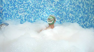 Banyoda bol köpüklü bir küvette yatarken sabun köpüğü üfleyerek kilden maske takan duygusal, sevimli bir adam. Komik bir kavram. Boşluğu kopyala