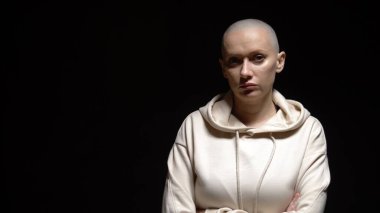 Kel, hamile bir kadın siyah arka planda kameraya bakıyor.