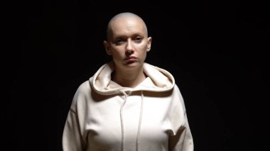 Kel, hamile bir kadın siyah arka planda kameraya bakıyor.