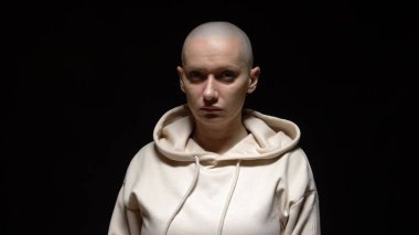 Kel, hamile bir kadın siyah arka planda kameraya bakıyor.