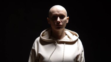 Kel bir kadın ne yazık ki kameraya bakar. Yüzünden aydınlıktan karanlığa ışık geçer. Siyah bir arkaplanda