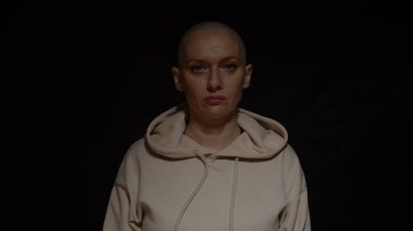 Kel bir kadın ne yazık ki kameraya bakar. Yüzünden aydınlıktan karanlığa ışık geçer. Siyah bir arkaplanda