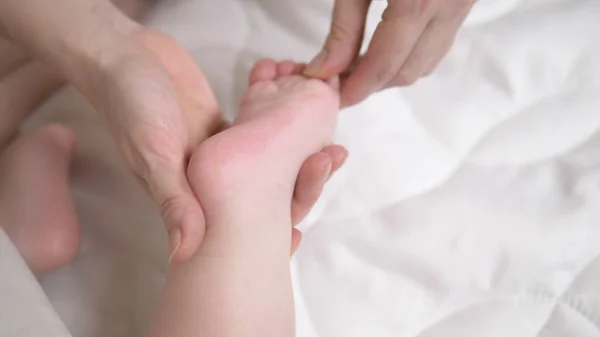 Τα γυναικεία χέρια κάνουν μασάζ στο μωρό στο κρεβάτι. κοντινό πλάνο — Φωτογραφία Αρχείου