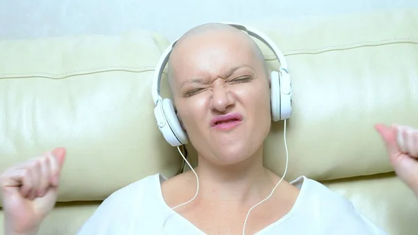 Close-up. uma mulher careca em fones de ouvido ouve música e move a cabeça para a batida da música . — Fotografia de Stock