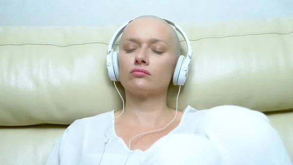 Close-up. uma mulher careca em fones de ouvido ouve música e move a cabeça para a batida da música . — Fotografia de Stock