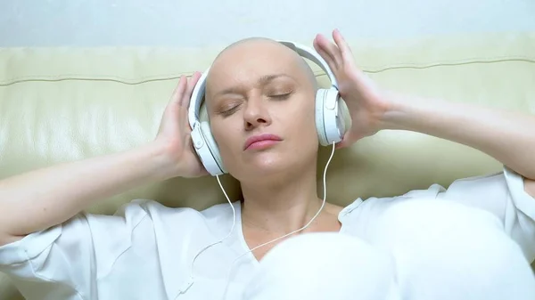 Close-up. a bald woman in headphones listens to music and moves her head to the beat of the music. — Stock Photo, Image