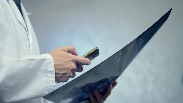 Nahaufnahme. Arzt hält Röntgenbild und Smartphone in der Hand — Stockfoto