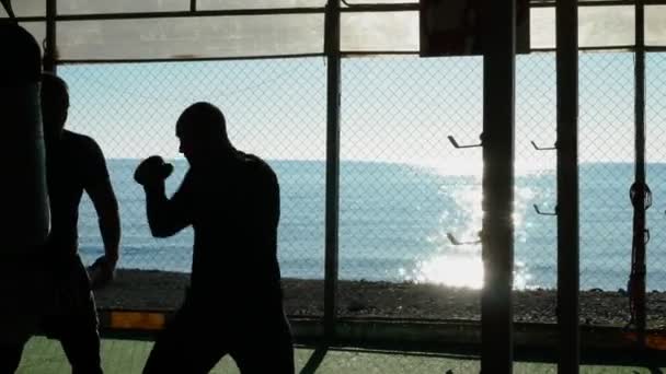Σιλουέτες. Δύο άνδρες πυγμάχος αθλητής προπονούνται σε ένα υπαίθριο γυμναστήριο σε μια παραλία κοντά στη θάλασσα. — Αρχείο Βίντεο