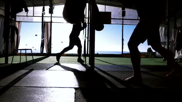 Närbild. Superlångsam rörelse. silhuetter. Två manliga boxare idrottare tränar i en utomhus gym på en strand nära havet. — Stockvideo