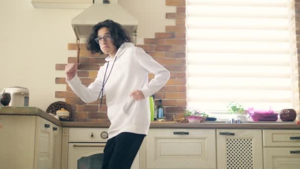 Gelukkig knap tiener jongen met lange krullend haar dansen in de keuken. — Stockvideo