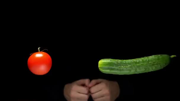 Fresh ripe red tomato and green cucumber levitate in the air on a black background, male hands applaud in the background. concept illusionist, levitation — ストック動画