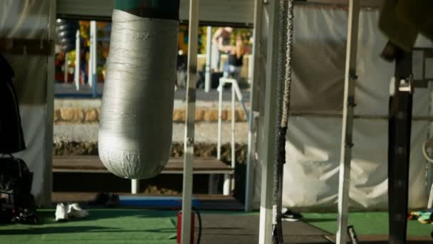 Blurred background. concept of outdoor playground on the street. in focus a punching punching bag, in the background blurry people are engaged in open air — ストック動画