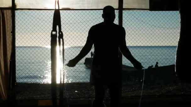 Silüet. Sportif adam açık havada salonda ip atlıyor kumsalda mavi deniz manzaralı ve açık gökyüzü — Stok video