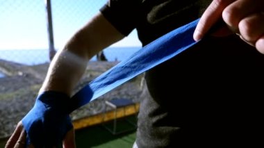 Yakın plan. Süper yavaş çekim. Silüet. Boksör maçtan önce elini elastik bir bandajla bandajlıyor. Sahildeki spor salonunda, mavi denizin üstünde.