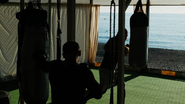 Silhuetter. Två manliga boxare idrottare tränar i en utomhus gym på en strand nära havet. — Stockfoto