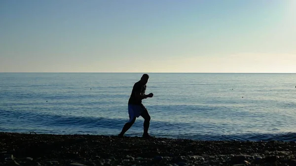 Silueta de un atleta boxeador en la playa contra el mar azul y el cielo despejado. boxeo de sombras — Foto de Stock