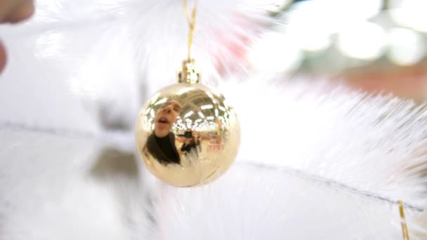 Nahaufnahme, männliche Lippen pusten auf eine goldene Kugel auf einem weißen künstlichen Weihnachtsbaum — Stockvideo
