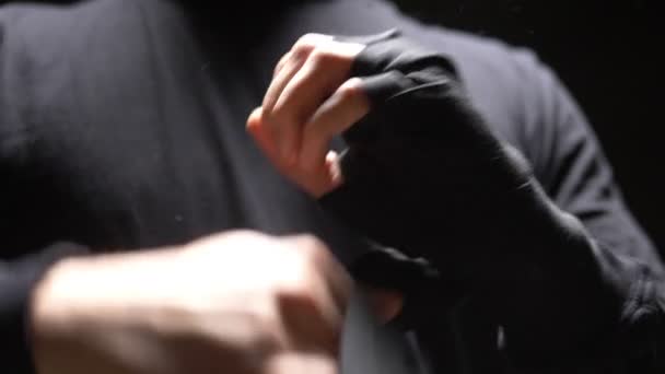 Een close-up. mannelijke handen gewikkeld rond een zwart elastisch verband aan de hand. zwarte achtergrond — Stockvideo