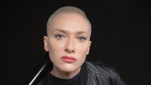 Mooie kortharige blonde vrouw in een zwart leren jasje met een honkbalknuppel op zwarte achtergrond — Stockvideo
