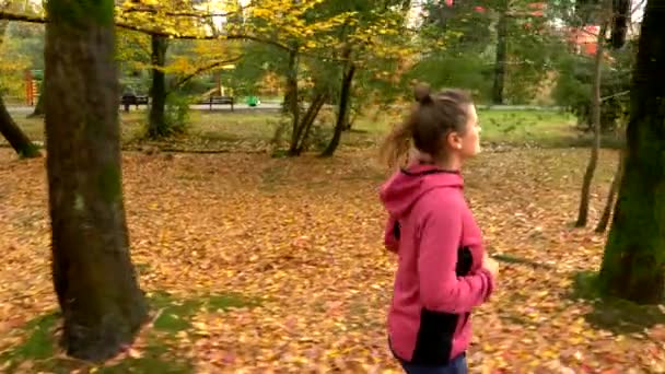 Krásná žena s dlouhými vlasy běhání v podzimním parku. boční pohled — Stock video